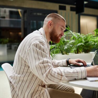 Side,View,Of,Concentrated,Adult,Man,Using,Laptop,And,Writing