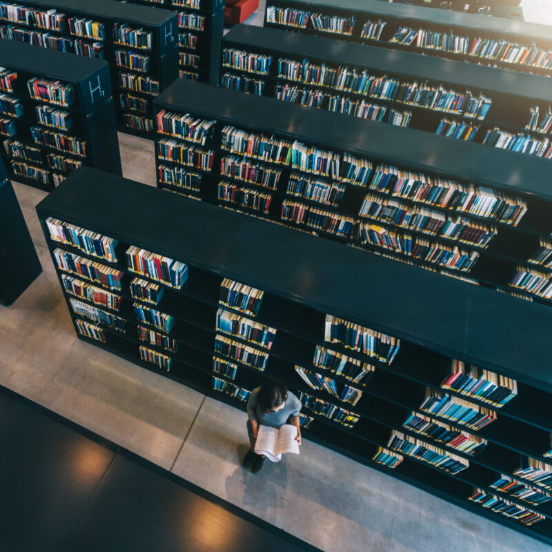 Female student at library bookshelf reading book